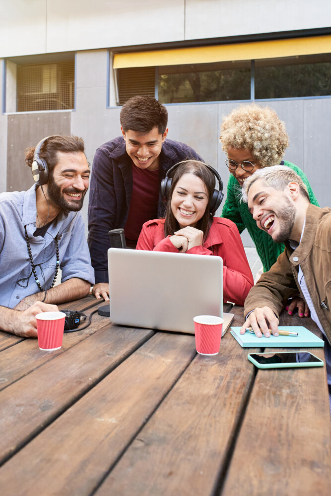 Vertical photo. Video call of a Group of young smiling people outdoors watching a video on the laptop. Colleagues broadcasting togethers SEOlaundry