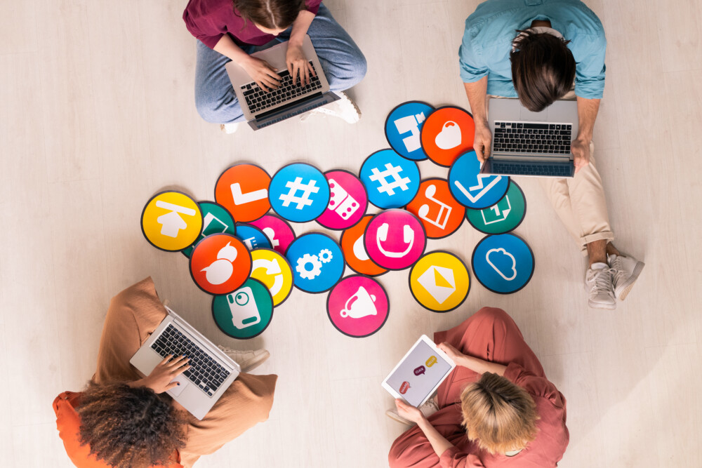 Young friendly people in casualwear sitting by multi-color papers with icons